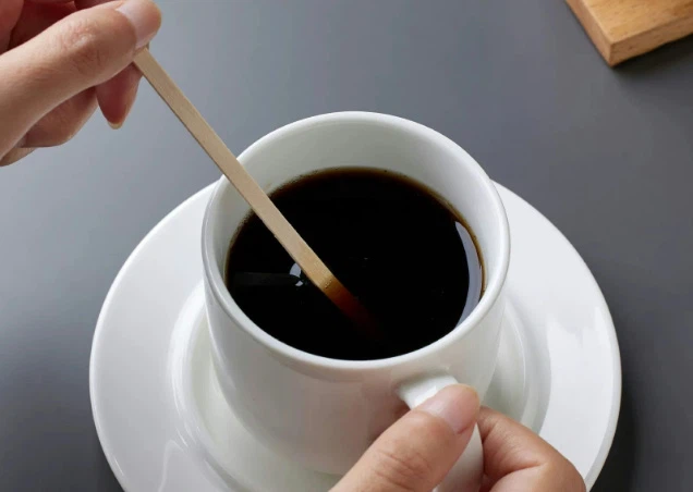 Hand stirring hot coffee with biodegradable wooden stirrer Hand stirring hot coffee with biodegradable wooden stirrer